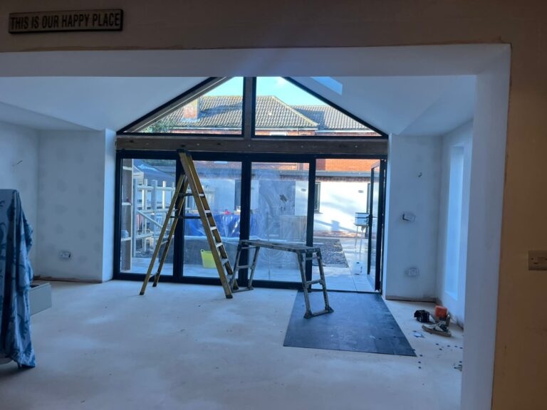 Bright, unfinished room with a ladder, scaffolding, and large glass doors leading to an outdoor space.