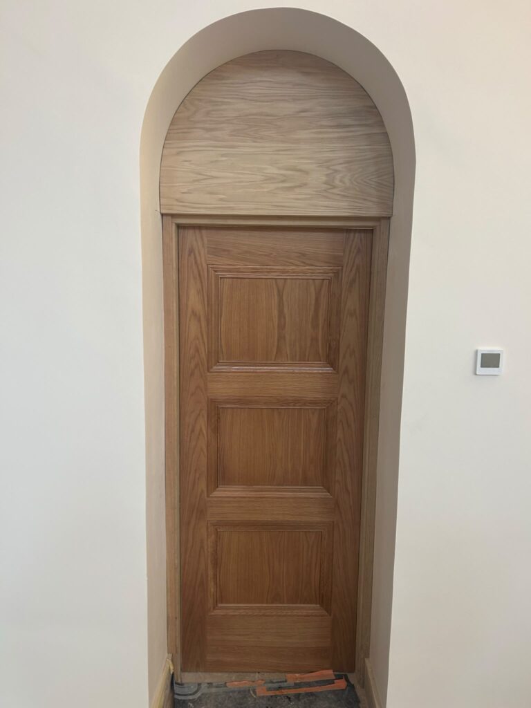 A grid of five photos showing an oak front door and its arched fanlight in various stages of installation. The main image is a full view, with four close-ups detailing the arch, door panels, and frame against white walls.