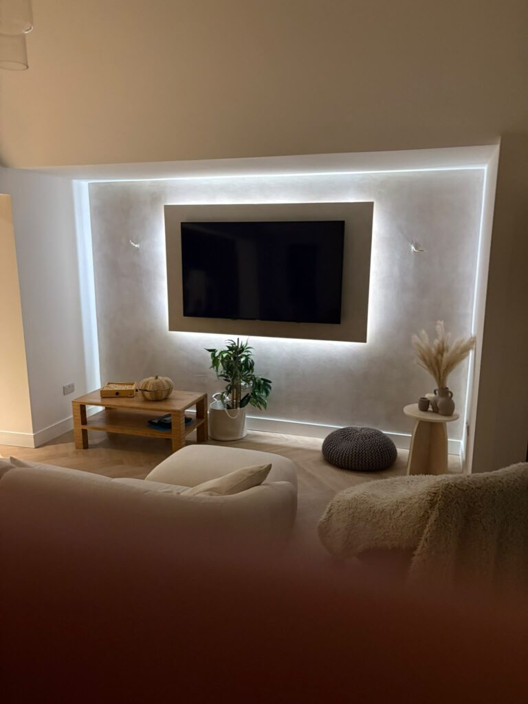 This image is a collage of several photos showing a modern living room interior. The main focus is a feature wall with a recessed space for a large flat-screen TV, which is framed by white molding and illuminated by hidden LED strip lighting. The wall